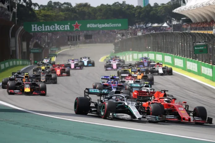 Sejumlah Mobil Formula 1 di Lintasan Balap Sejumlah mobil Formula 1 melaju berdekatan di lintasan balap dengan tribun penonton di belakangnya.
