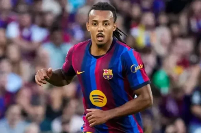 Jules Kounde dalam Seragam Barcelona Jules Kounde mengenakan seragam Barcelona dengan latar belakang penonton di tribun.