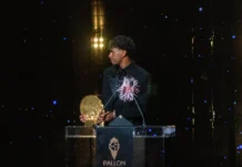 Lamine Yamal Jadi Pemain Muda Terbaik Tiga Tahun Beruntun Seorang pesepak bola muda mengenakan jas hitam memegang trofi emas di podium Ballon d'Or