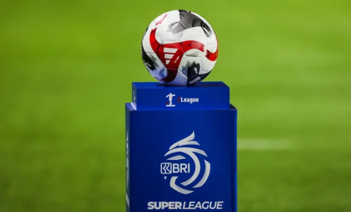 Bola pertandingan di atas dudukan biru berlogo BRI Super League di lapangan sepak bola